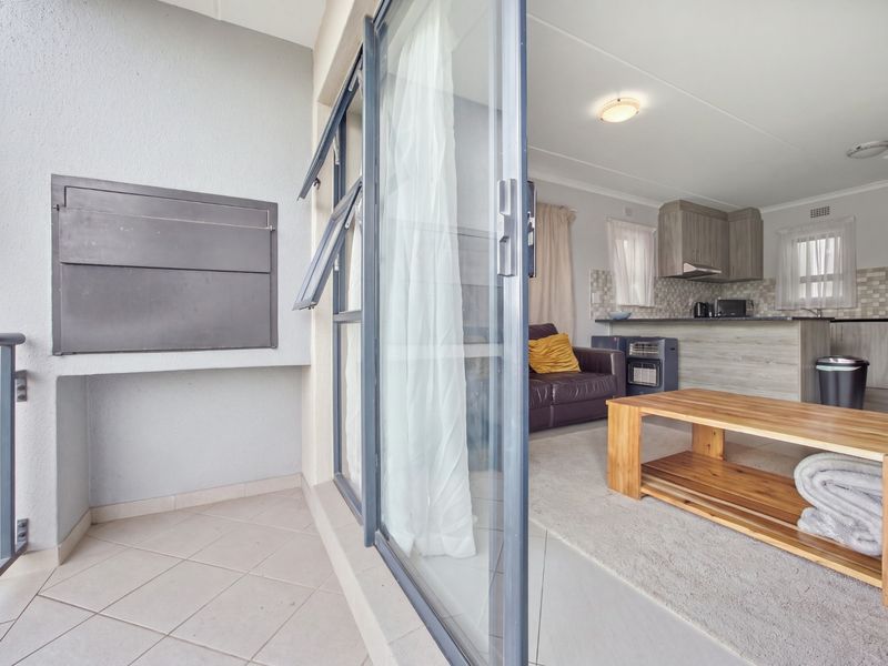 A covered balcony featuring a built-in braai and tiled flooring, providing seamless access to the open-plan living and kitchen area.