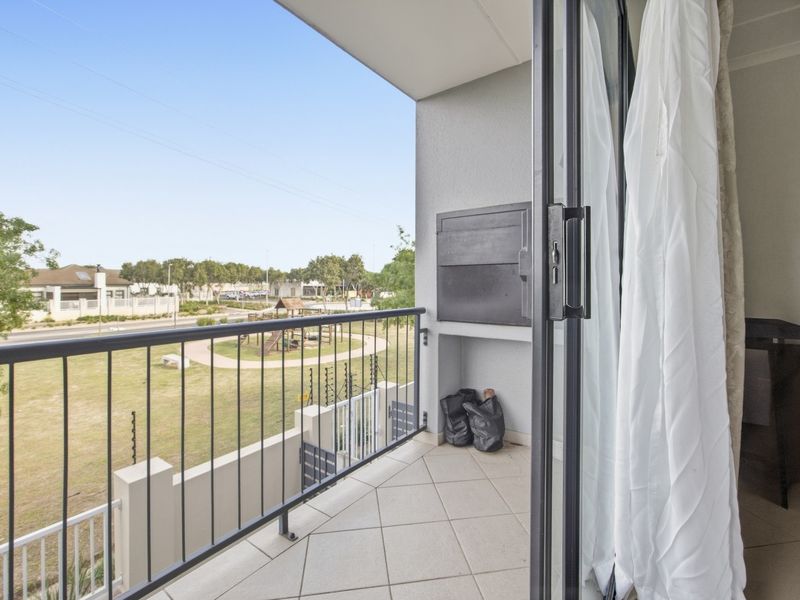 A covered balcony featuring tiled flooring, a built-in braai, and a metal balustrade, offering views over the complex grounds.