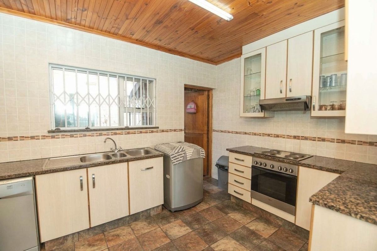 A functional kitchen featuring built-in cabinetry, granite countertops, a double sink, and integrated cooking appliances, finished with a timber ceiling and tiled flooring.
