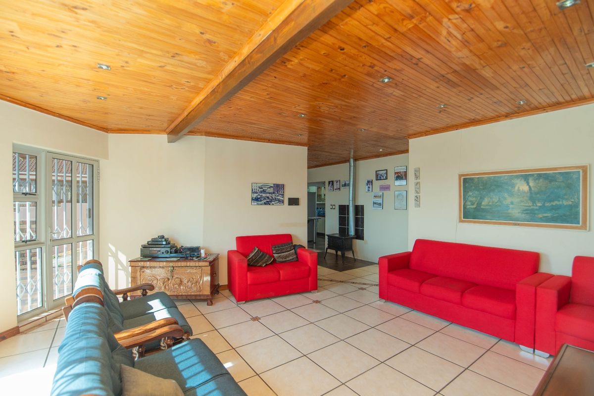 Spacious living area featuring a warm timber-clad ceiling, ceramic tiled flooring, and a functional freestanding wood-burning stove with direct access to the patio.