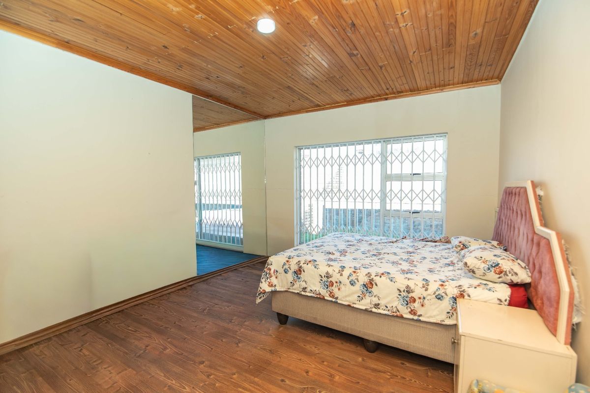 A bedroom featuring timber-clad ceilings, laminate flooring, and security gates on the windows.