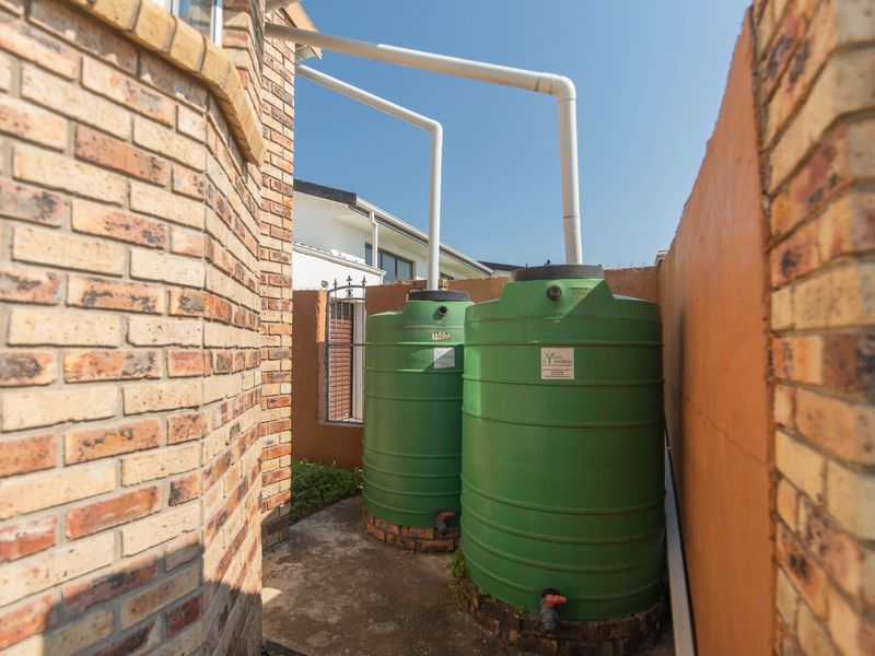 Side yard utility area featuring two green water storage tanks connected to the building's gutter system on a concrete base.