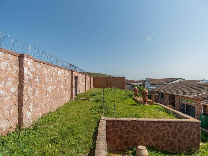 A rear garden area featuring a perimeter wall with security razor wire, a low retaining wall, and views of neighboring residential tiled roofs.