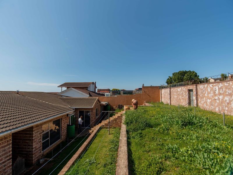 Rear view of the property featuring a brick facade, tiled roof, and a large garden area enclosed by a high perimeter wall with security wire.