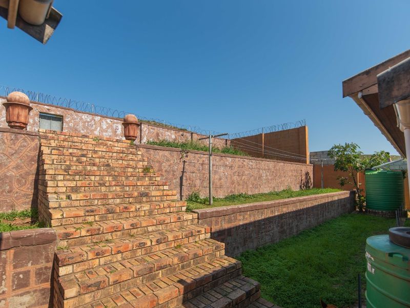 Rear garden area featuring a brick staircase, retaining walls, perimeter security fencing with razor wire, and installed water storage tanks.