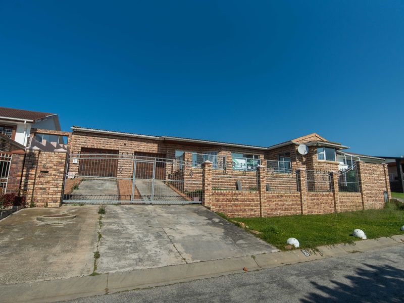 Front exterior view of a single-story face brick house featuring a double garage, paved driveway, and secure perimeter walling.