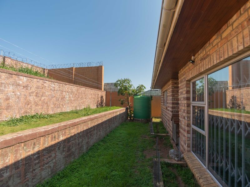 Rear exterior view of the property featuring a brick facade, retaining wall with security fencing, and a water tank in the garden area.