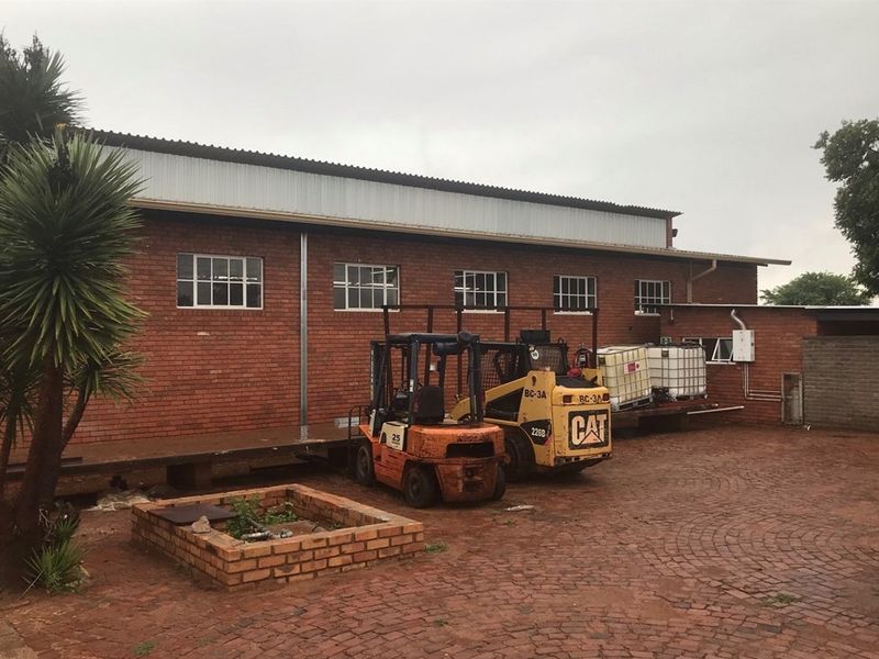 Rear view of a farm utility building featuring a brick facade, metal roofing, and a paved courtyard area with a raised loading platform.