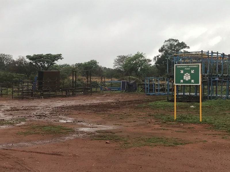 An outdoor utility area on the farm featuring an emergency assembly point sign and various metal storage structures on unpaved ground.