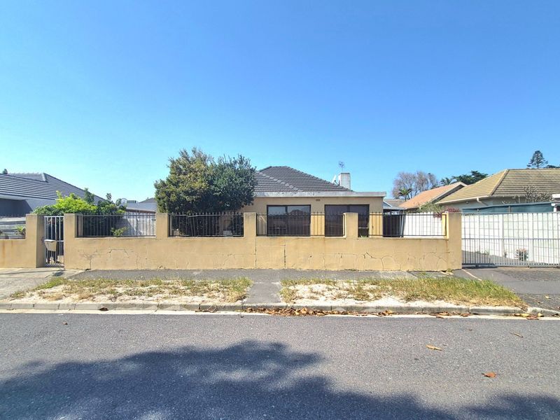 Front exterior view of a single-story house featuring a perimeter wall with metal fencing, a sliding gate, and a tiled roof.