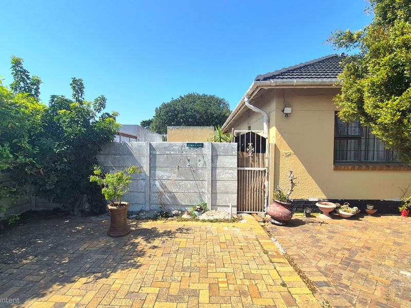 Rear exterior view featuring a paved patio area, precast concrete boundary wall, and side access gate leading to the main house structure.