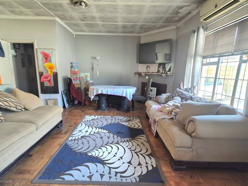 A living room featuring parquet flooring, a wall-mounted air conditioner, and large windows. The ceiling shows visible signs of water damage and peeling paint.
