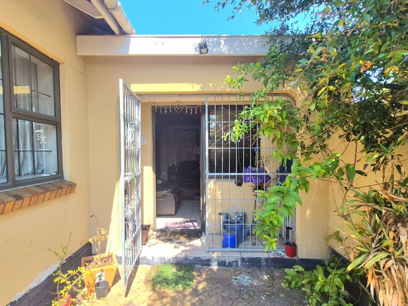 Rear exterior view showing a paved patio area with security gate access to the home and established garden foliage.