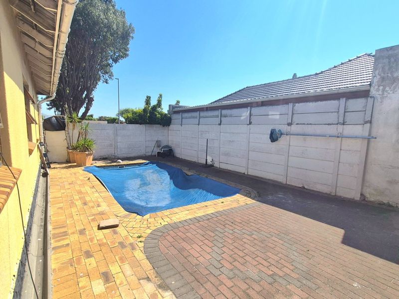 Outdoor pool area featuring a covered swimming pool, brick paved surround, and enclosed by a precast concrete boundary wall.