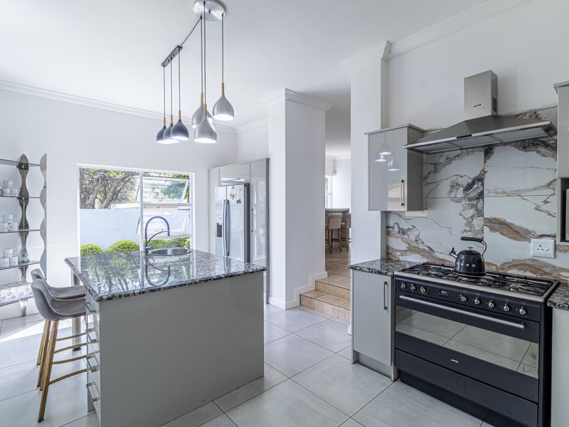 Modern kitchen featuring a central island with granite countertops, gas stove, integrated extractor, and elegant marble-look splashback with high-quality finishes.