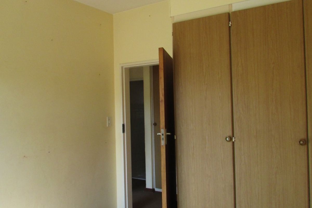 An empty bedroom featuring built-in wooden cupboards, carpeted flooring, and a simple pendant light fixture, ready for renovation or staging.