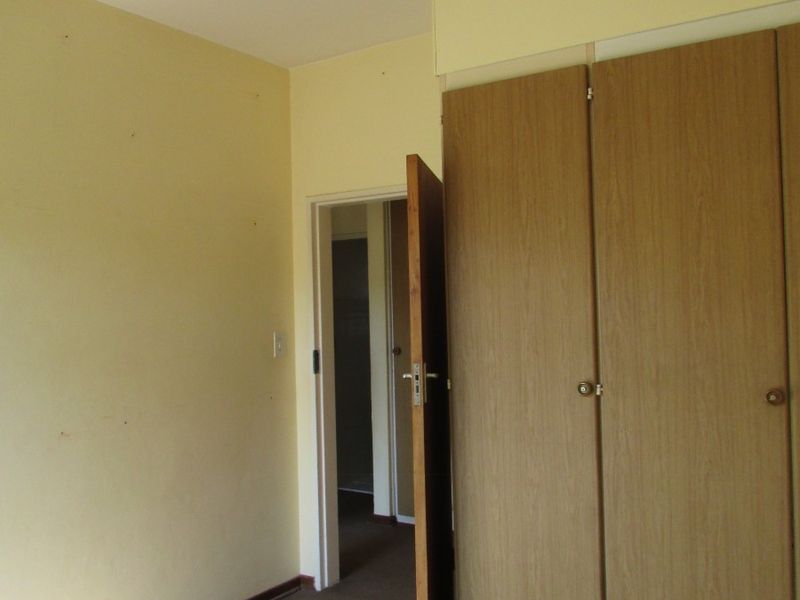 An empty bedroom featuring built-in wooden cupboards, carpeted flooring, and a simple pendant light fixture, ready for renovation or staging.