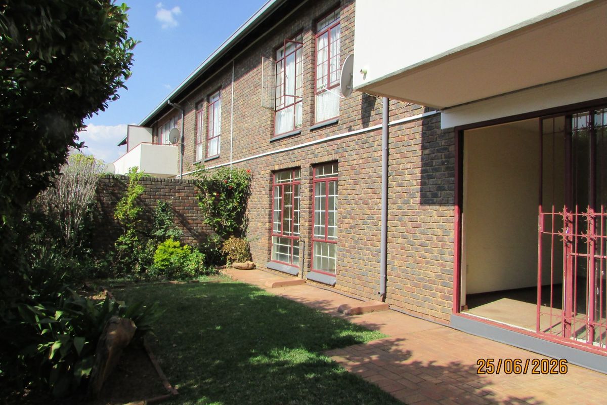 Rear view of the apartment building featuring a face brick facade, paved patio area, and a small private garden space.