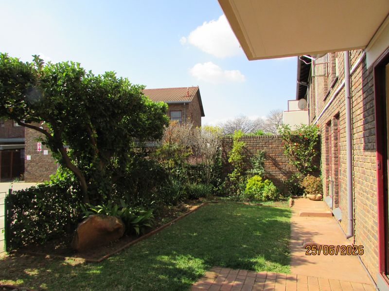 A private rear garden area featuring a small lawn, paved walkway, and facebrick boundary wall, accessible from the apartment's covered patio.