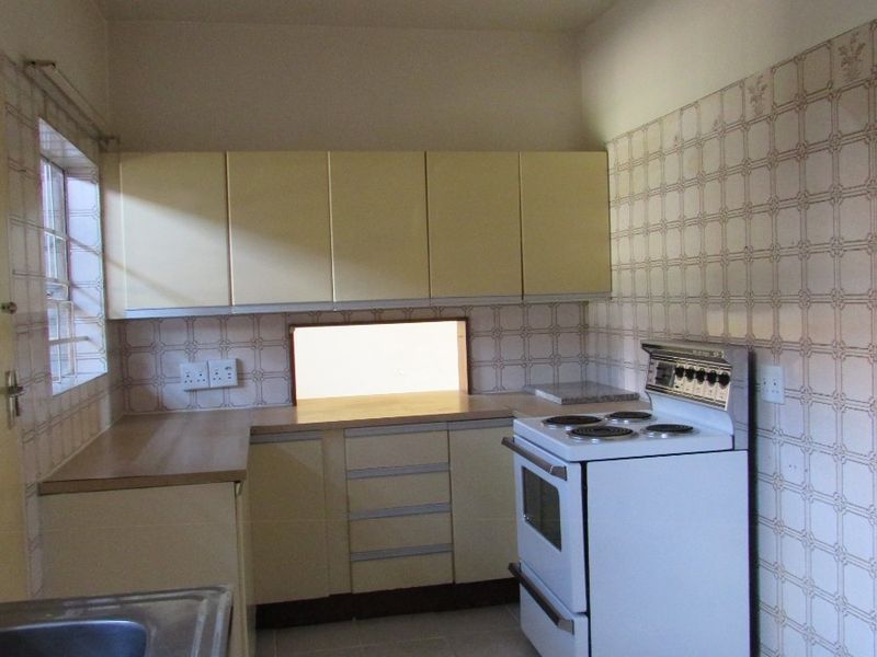 A functional kitchen featuring dated cabinetry, laminate countertops, a stainless steel sink, and a freestanding stove with tiled walls.