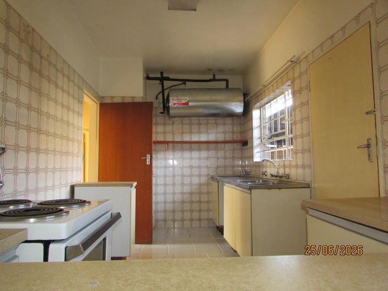 A functional kitchen featuring tiled walls, built-in cabinetry, a stainless steel sink, and an electric stove, offering a blank canvas for modern renovation.