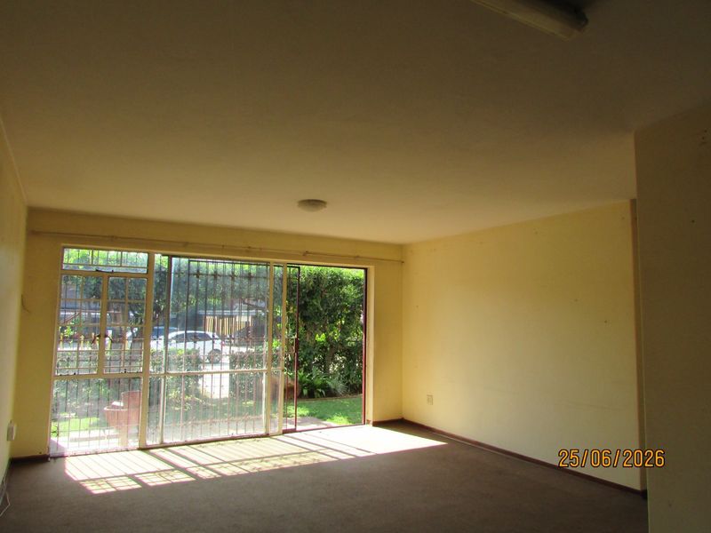 An empty living room featuring carpeted flooring and a large sliding glass door with security bars, providing direct access to the garden area.