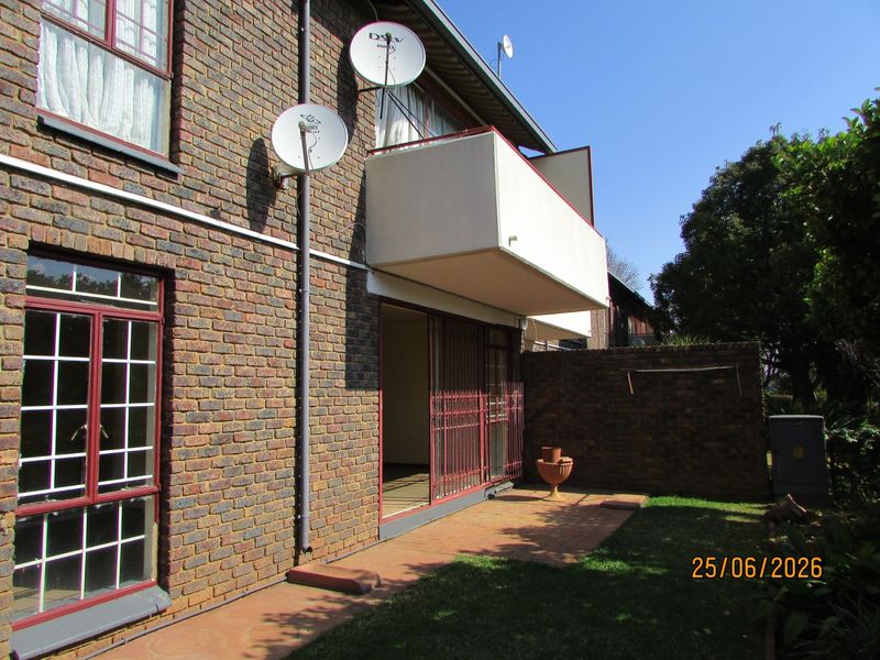 Rear view of the apartment building featuring a face brick facade, a private balcony, and a paved patio area leading to the garden.