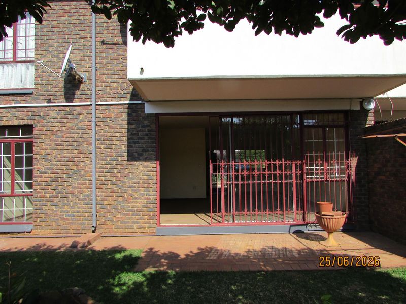 Ground floor patio area featuring brick facade, paved flooring, and a red metal security gate providing access to the interior.