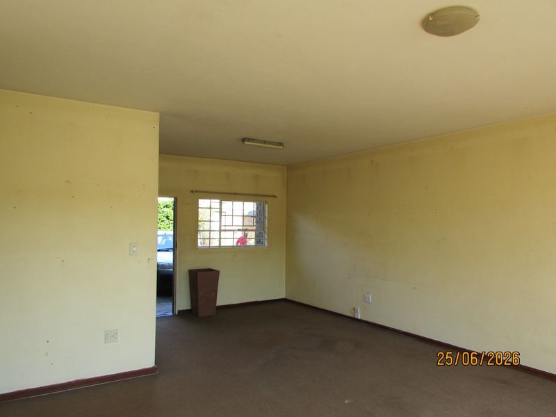 An empty living room featuring carpet flooring, metal security window bars, and basic lighting fixtures, requiring cosmetic updates to the walls and flooring.