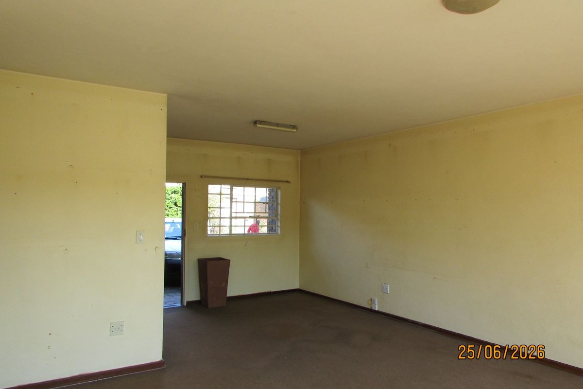 An empty living room featuring carpet flooring, metal security window bars, and basic lighting fixtures, requiring cosmetic updates to the walls and flooring.