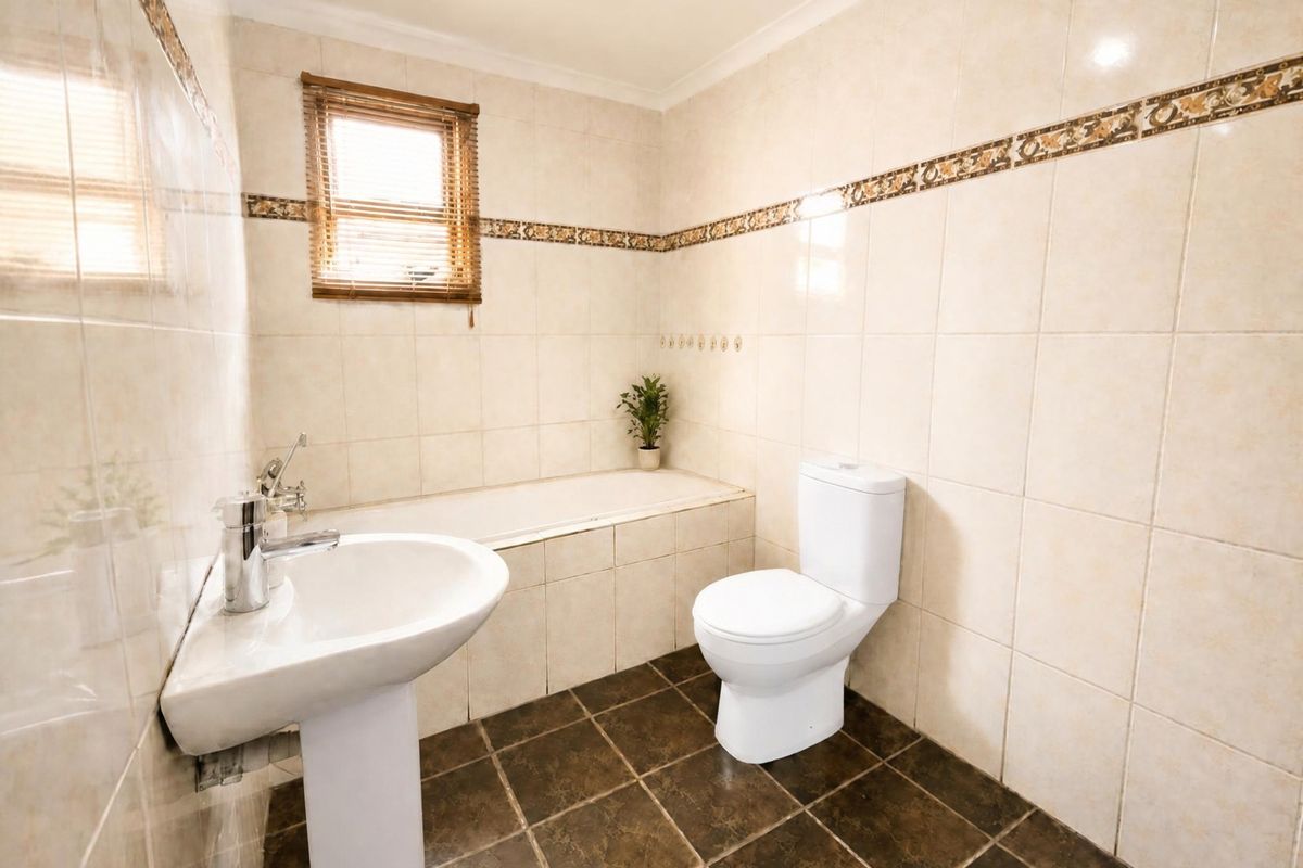 A functional bathroom featuring a pedestal basin, built-in bathtub, and toilet, finished with neutral wall tiles and dark floor tiles.