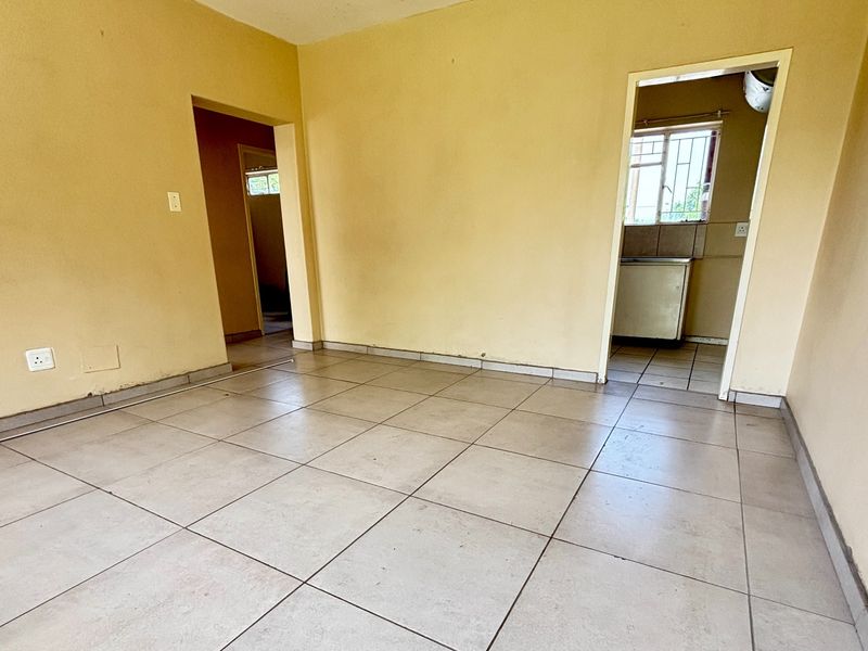 An empty living area featuring neutral ceramic floor tiles and yellow-toned walls, providing a blank canvas for potential interior updates.