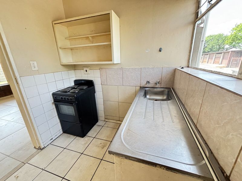 A compact, dated kitchen featuring a stainless steel sink, tiled splashbacks, and a freestanding electric stove, offering potential for modernization.