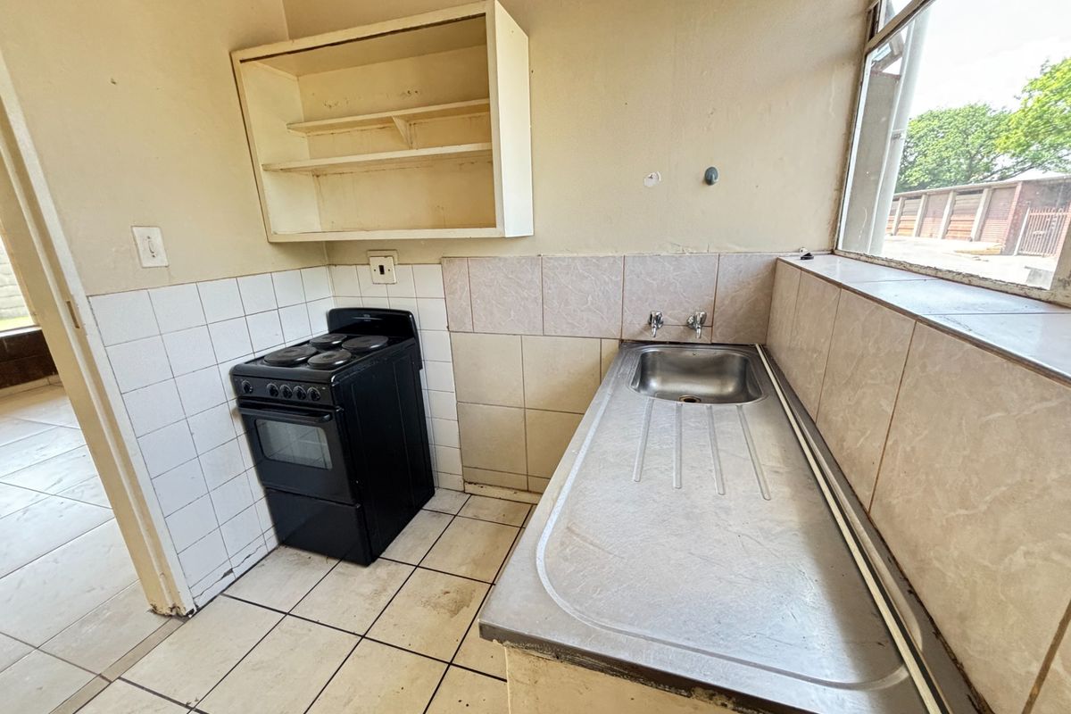 A compact, dated kitchen featuring a stainless steel sink, tiled splashbacks, and a freestanding electric stove, offering potential for modernization.