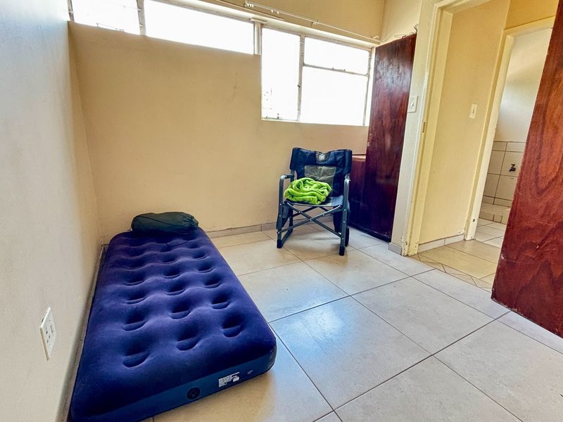 A simple bedroom featuring tiled flooring, high-level windows, and a built-in cupboard, offering a blank canvas for potential interior updates.