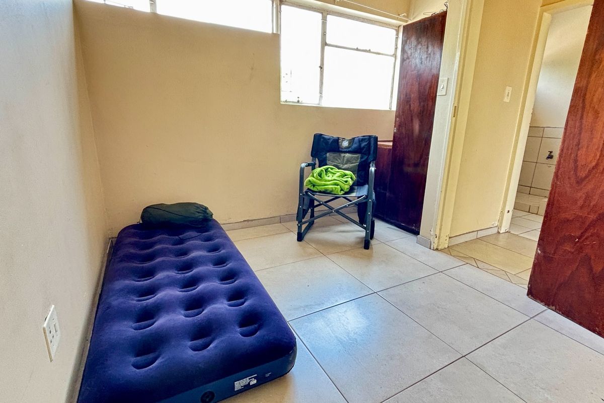 A simple bedroom featuring tiled flooring, high-level windows, and a built-in cupboard, offering a blank canvas for potential interior updates.