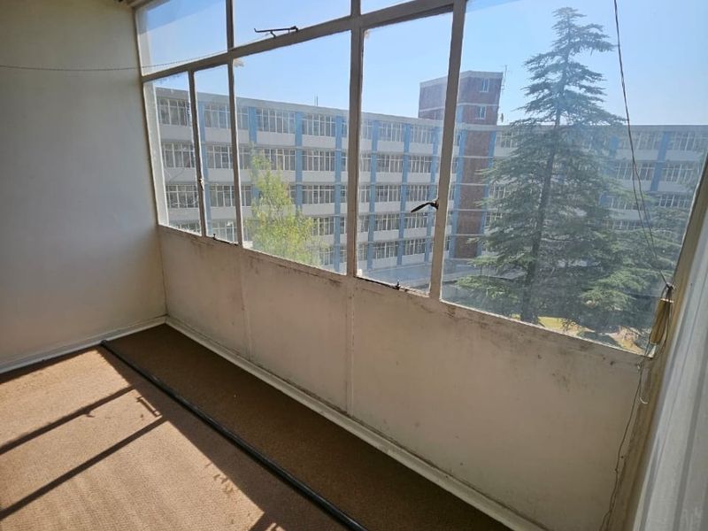An enclosed balcony featuring large windows with an urban view, offering a versatile space that could be updated with modern flooring and finishes.