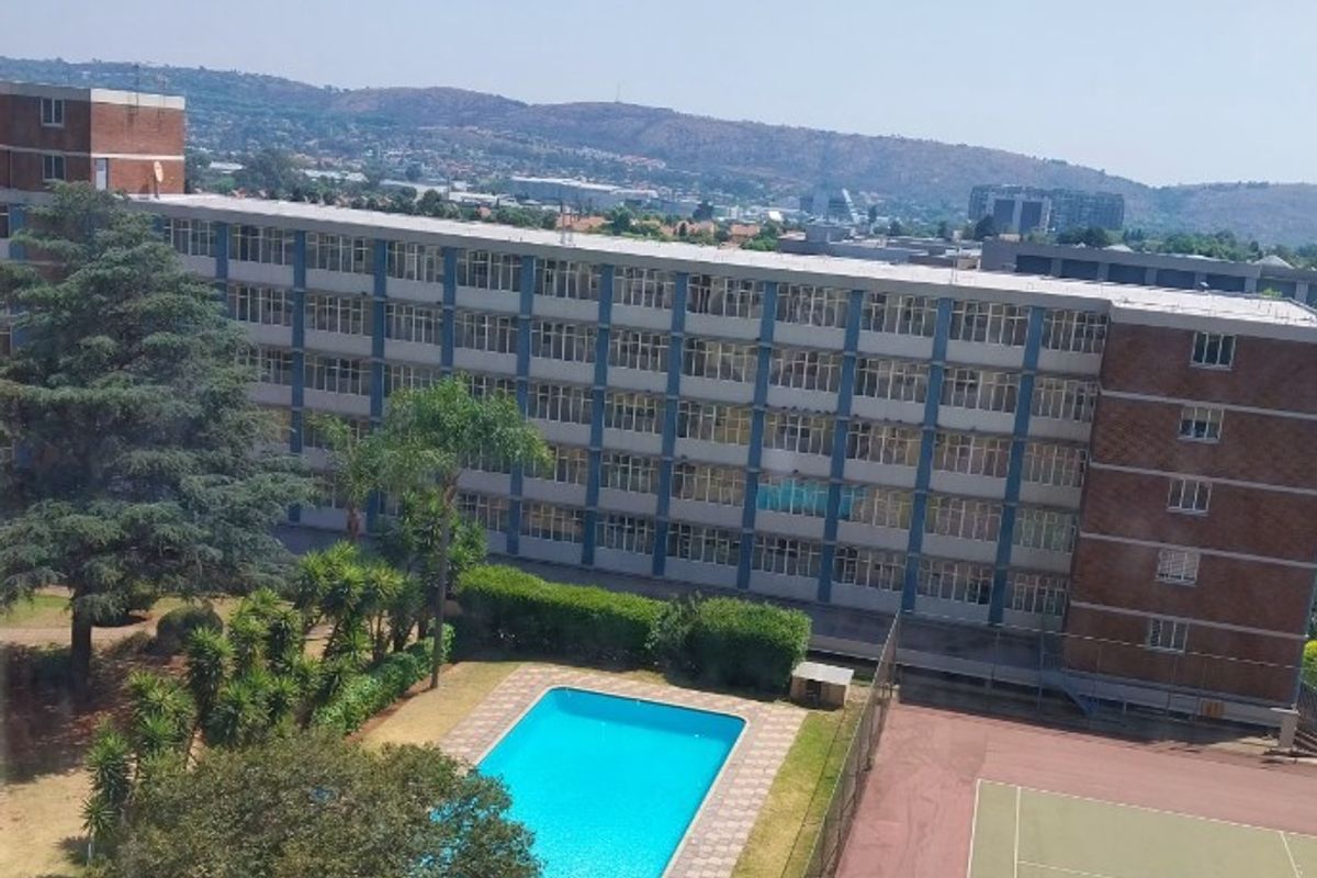 Elevated aerial view of the complex grounds featuring a swimming pool, tennis court, and surrounding landscaped areas.