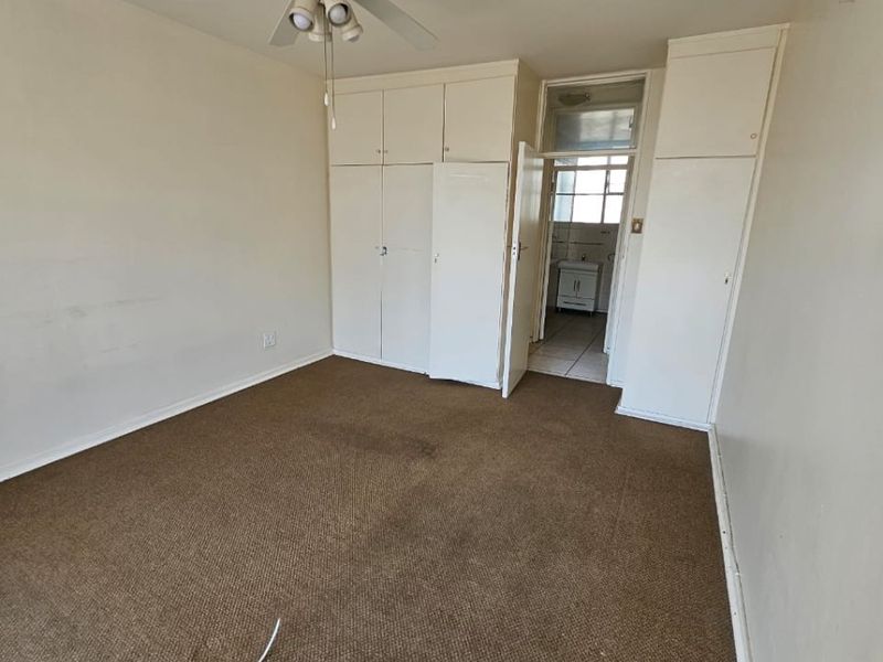 An empty bedroom featuring built-in cupboards, a ceiling fan, and carpet flooring, with an adjoining bathroom visible through the doorway.