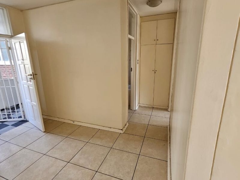 A vacant hallway featuring neutral tiled flooring and built-in storage cupboards, providing access to adjacent rooms and an exterior entrance.