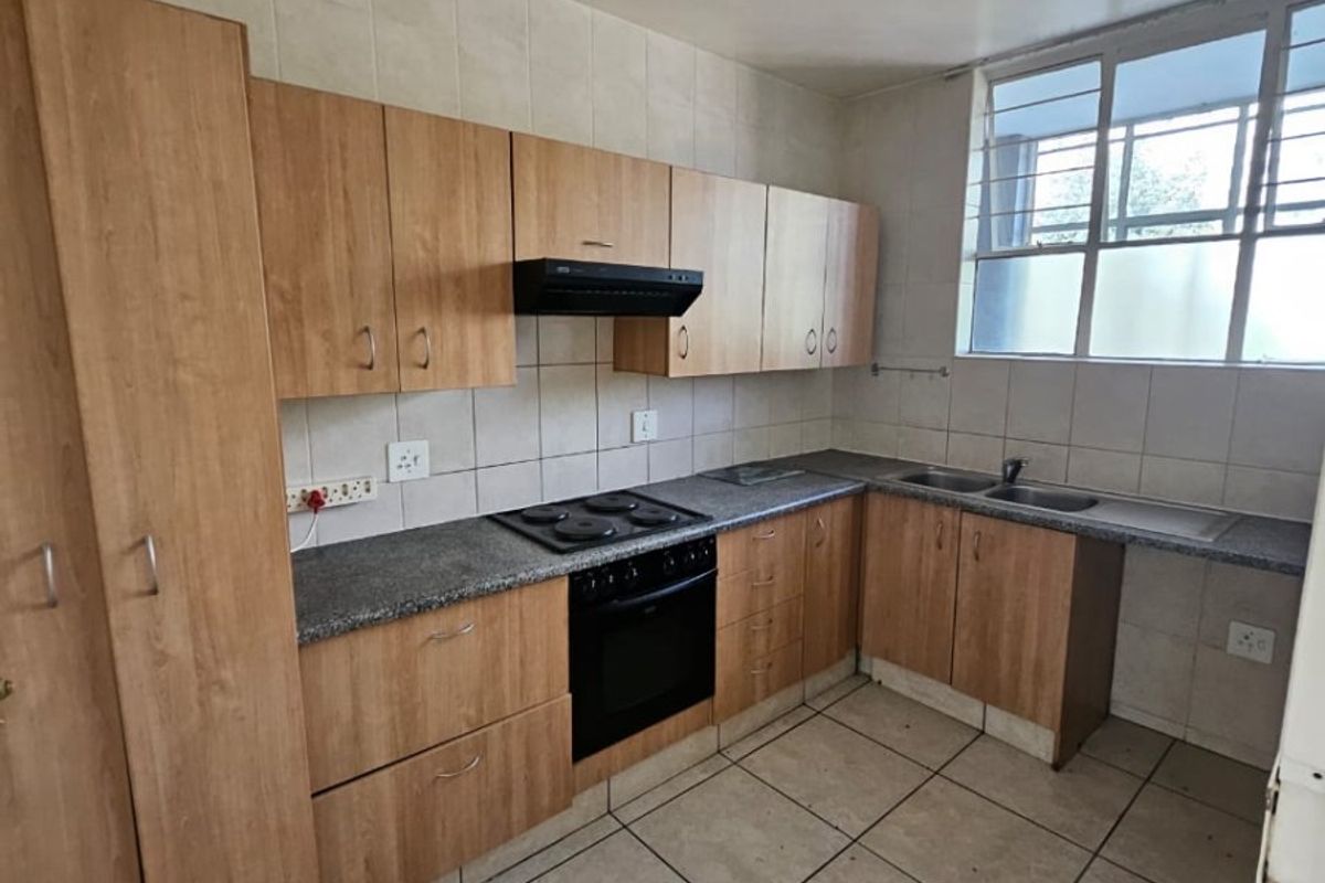 A functional kitchen featuring light wood-finish cabinetry, granite-look countertops, an integrated oven and hob, and tiled flooring throughout.