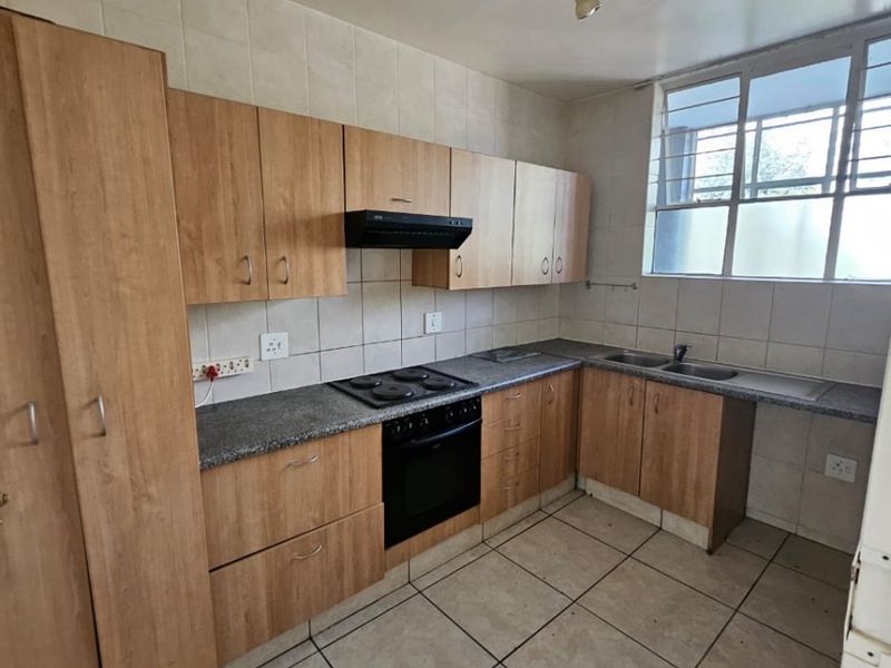 A functional kitchen featuring light wood-finish cabinetry, granite-look countertops, an integrated oven and hob, and tiled flooring throughout.