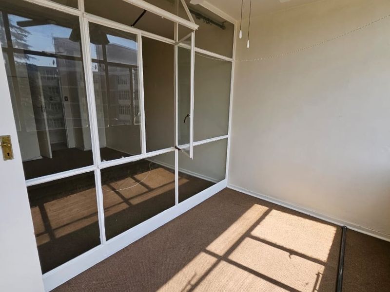 An enclosed balcony or sunroom featuring carpeted flooring, a ceiling fan, and a large glass partition wall with a visible crack.