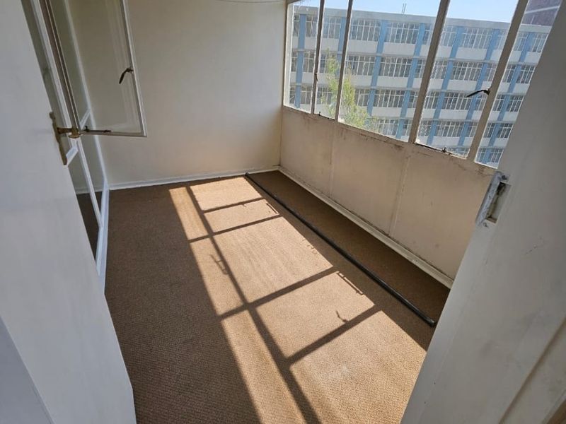 An enclosed balcony or sunroom featuring large windows, a ceiling fan, and carpeted flooring, offering a bright space with potential for modernization.