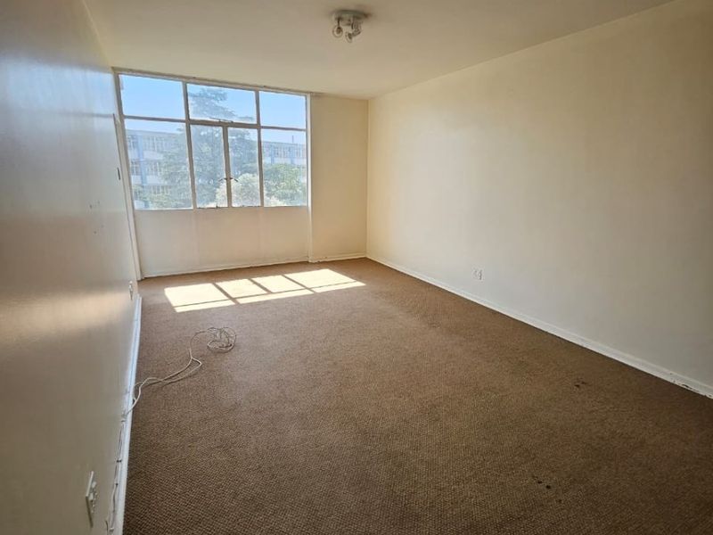 An empty, carpeted bedroom featuring a large window that provides natural light, ready for renovation or staging.