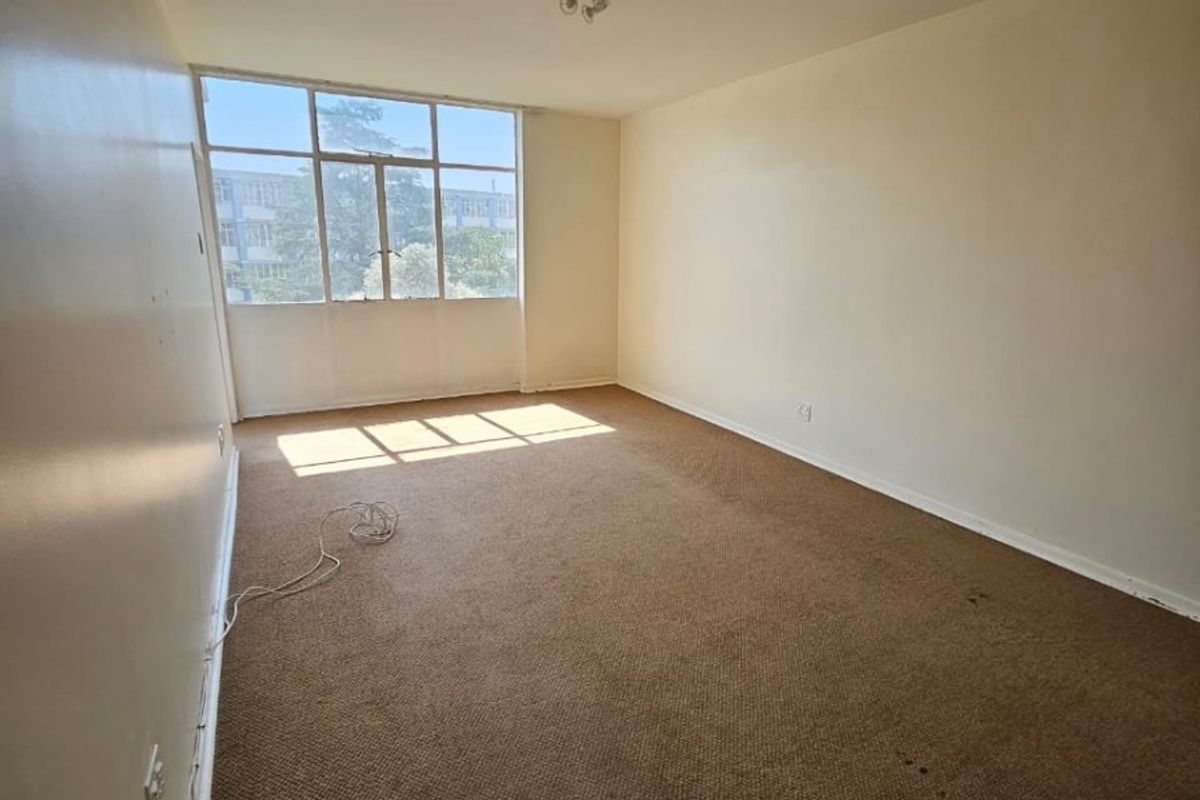 An empty, carpeted bedroom featuring a large window that provides natural light, ready for renovation or staging.