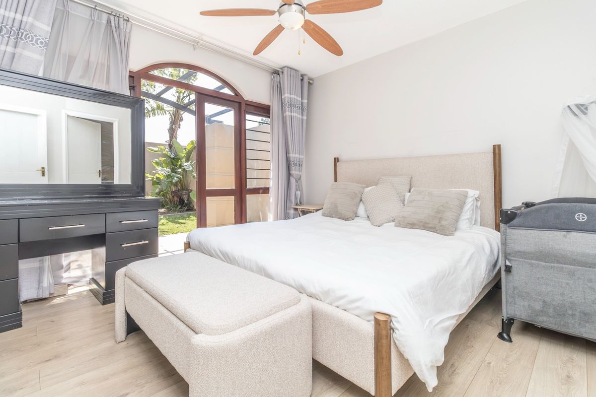 A bright bedroom featuring laminate flooring, a ceiling fan, and an arched glass sliding door providing direct access to the outdoor area.