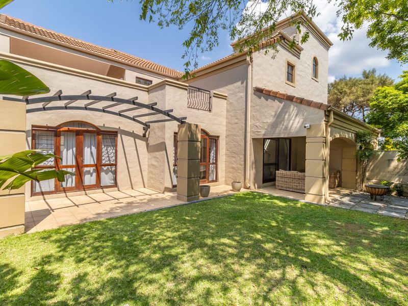 A well-maintained rear exterior view of a townhouse featuring a tiled patio, pergola, and a lush green garden.
