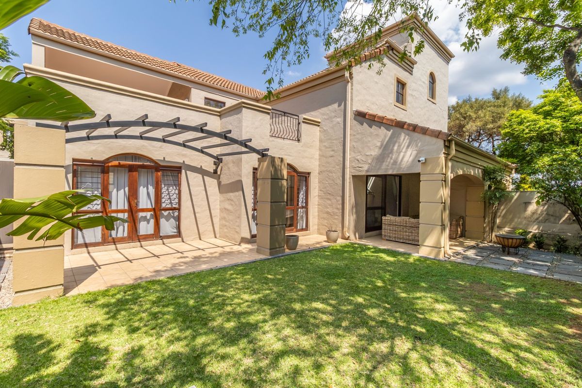 A well-maintained rear exterior view of a townhouse featuring a tiled patio, pergola, and a lush green garden.