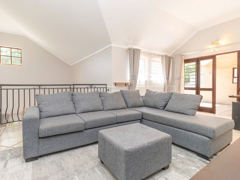 A bright living room featuring a vaulted ceiling, tiled floors, and a wrought iron balustrade, with direct access to an outdoor patio area.